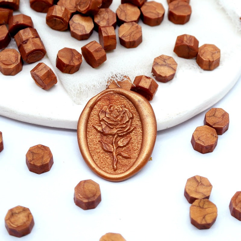 Some copper gold wax beads placed on white cushion and cloth, and an wax seal created with them.