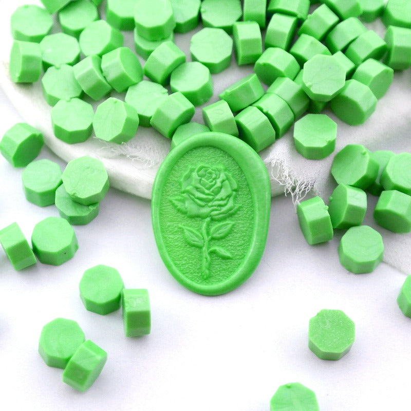 Some jade green wax beads placed on white cushion and cloth, and an wax seal created with them.