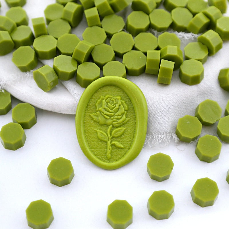 Some olive green wax beads placed on white cushion and cloth, and an wax seal created with them.