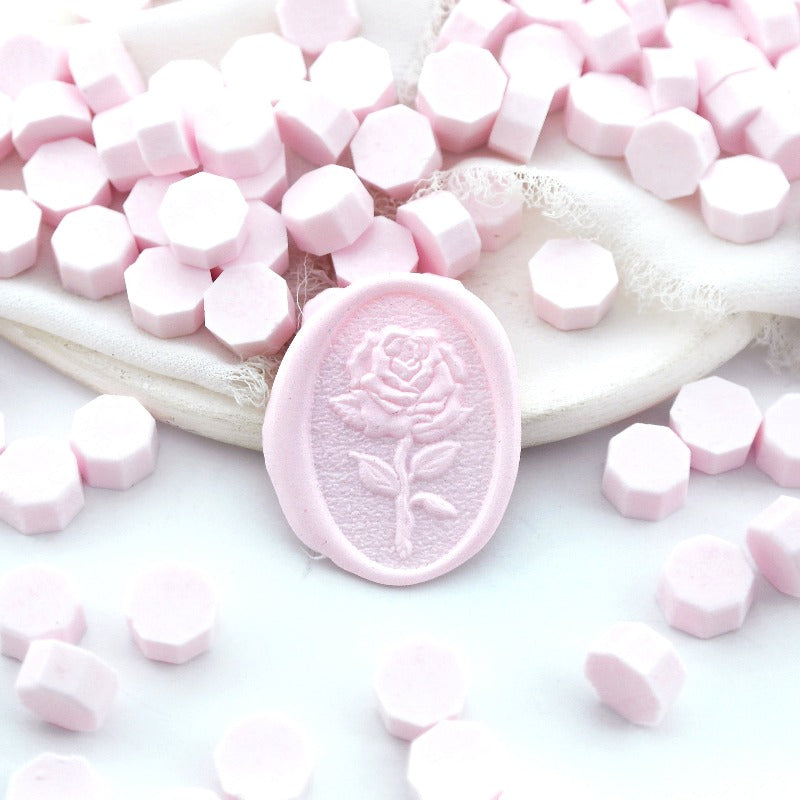 Some light pink wax beads placed on white cushion and cloth, and an wax seal created with them.