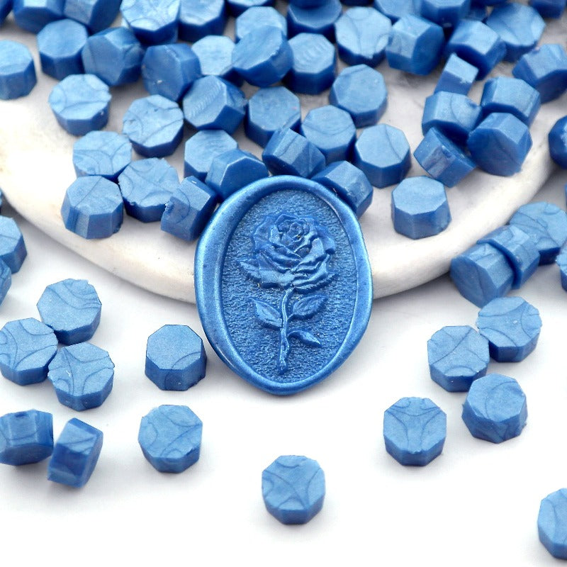 Some pearlescent ocean blue wax beads placed on white cushion and cloth, and an wax seal created with them.