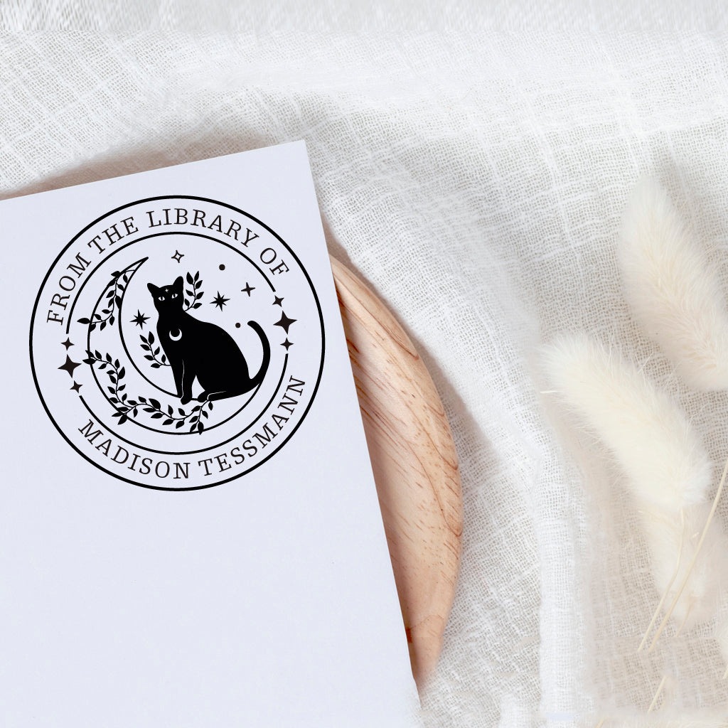 A personalized book stamp in round, the top is text -from the library of, the centre is graphic of leaves, moon,stars and black cat , the bottom is to custom your name.