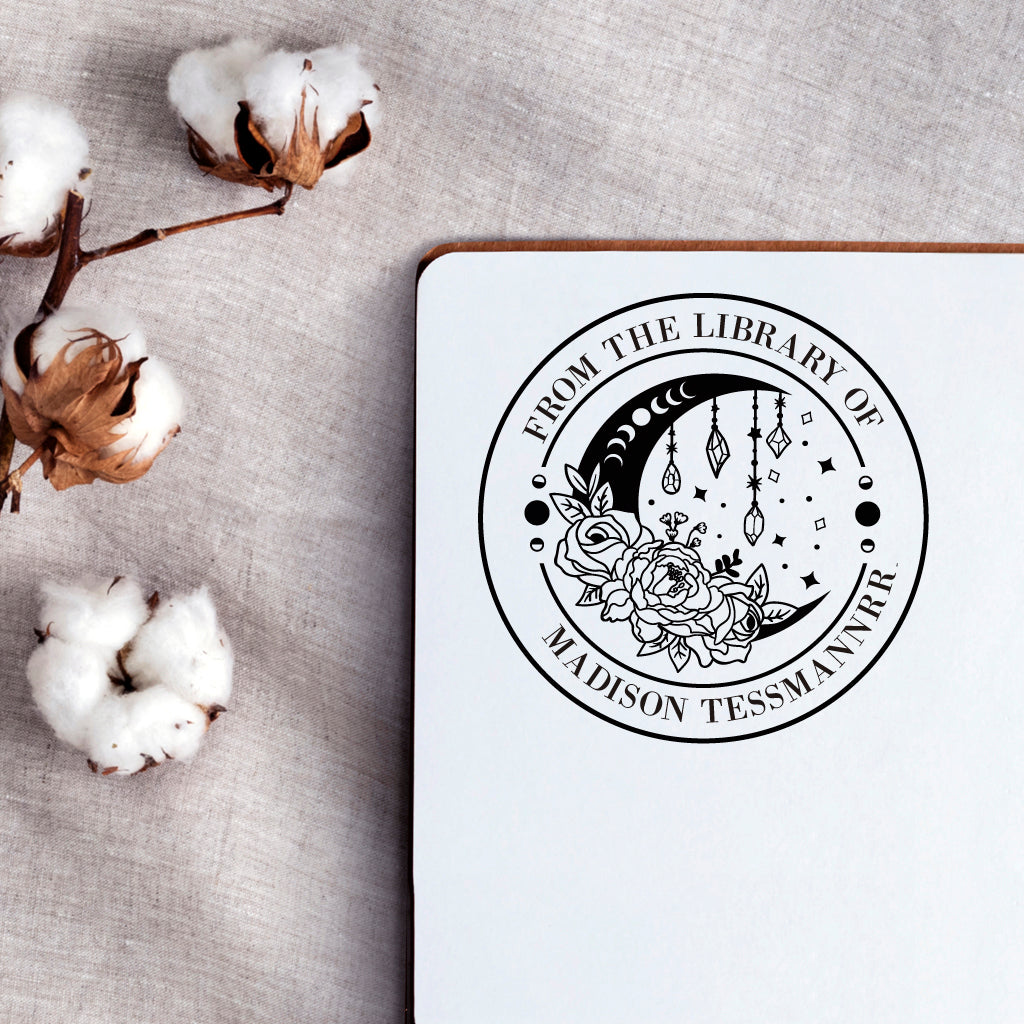 A personalized book stamp in round, the top is text -from the library of, the centre is the graphic of moon phases, diamond and rose flower, the bottom is to custom your name.