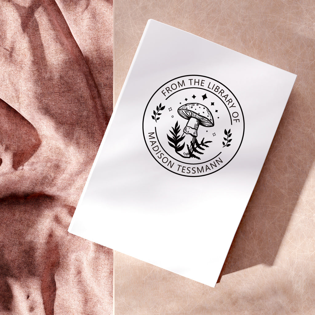 A custom Library Stamp, personalized with your text and mushroom pattern, stamped in black on a white book.