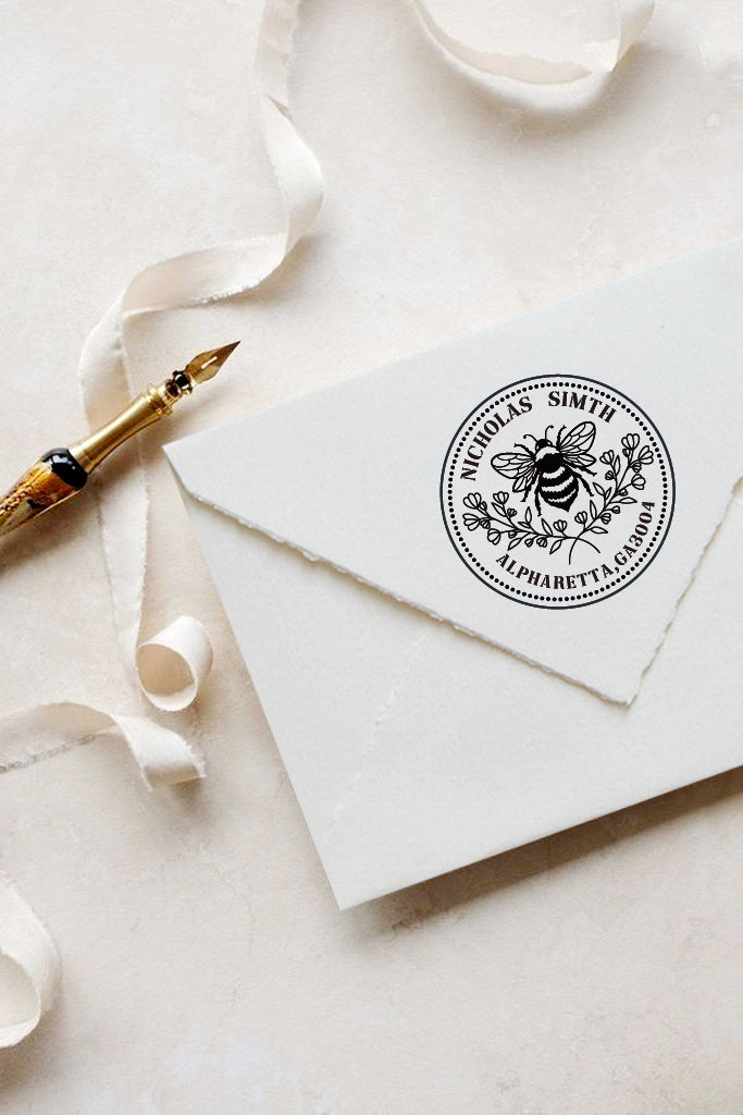 A personalized self inking address stamp, customized with your name and address, bee and flower, stamped on the white envelop, beside it, a ribbon is waiting for packing the gift.