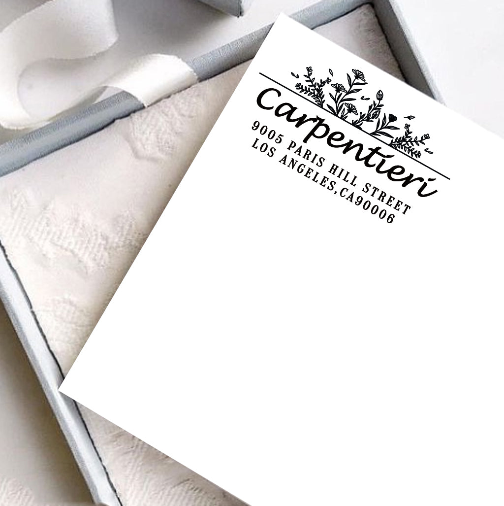 A personalized self inking address stamp, customized with your name, address and flower, stamped on the white card, a gift box is under it.
