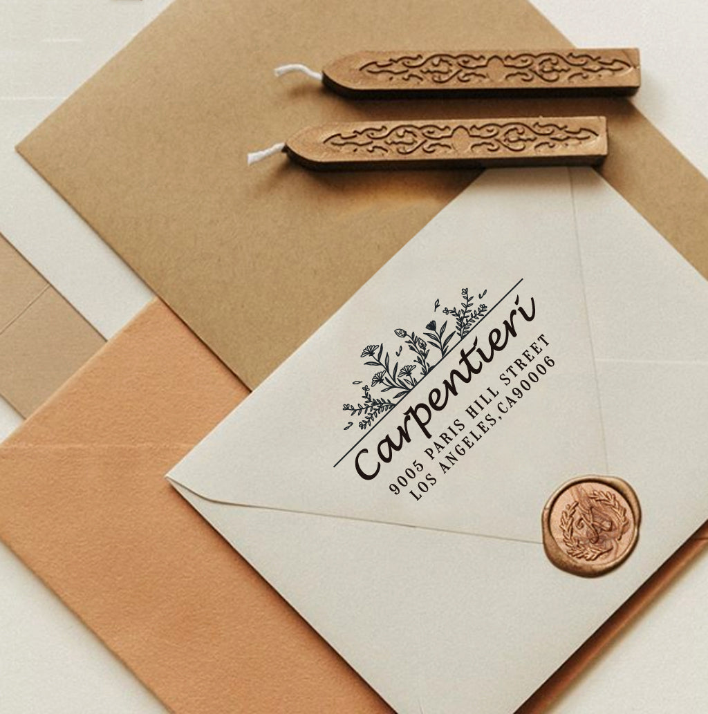 A personalized self inking return address stamp, customized with your name, address and flower, stamped on the white envelope, beside it, sealing wax is creating a wax seal on the mail.