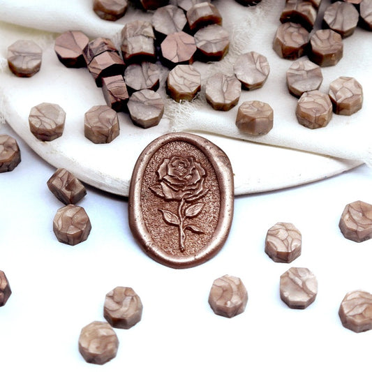 Some Champagne gold wax beads placed on white cushion and cloth, and an wax seal created with them.