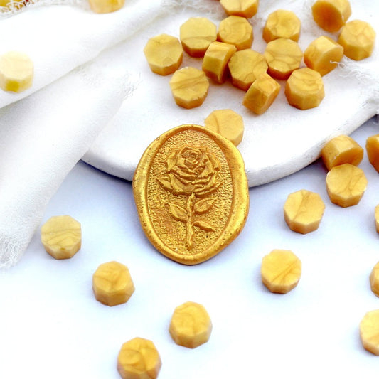 Some gold wax beads placed on white cushion and cloth, and an wax seal created with them.