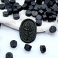 Some black wax beads placed on white cushion and cloth, and an wax seal created with them.