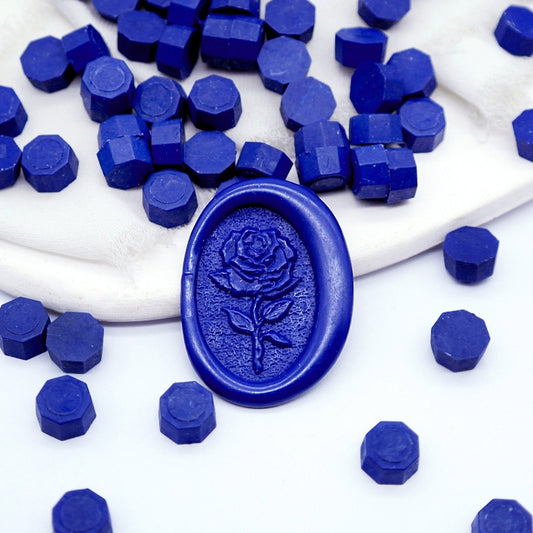 Some midnight blue wax beads placed on white cushion and cloth, and an wax seal created with them.