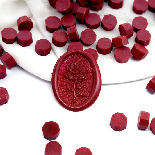 Some Burgundy Red wax beads placed on white cushion and cloth, and an wax seal created with them.
