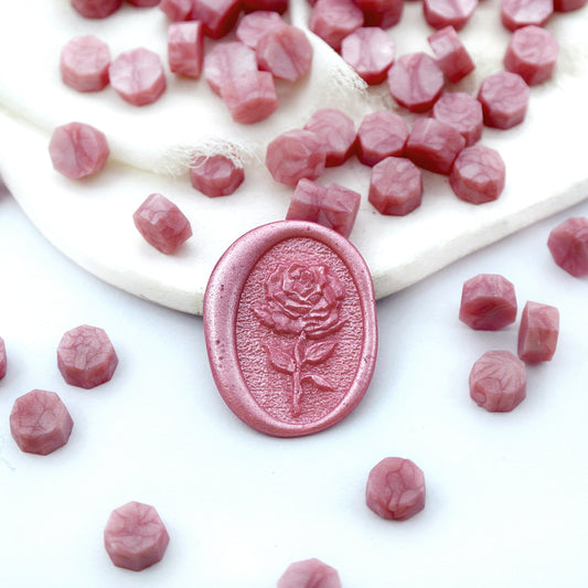 Some rose pink wax beads placed on white cushion and cloth, and an wax seal created with them.
