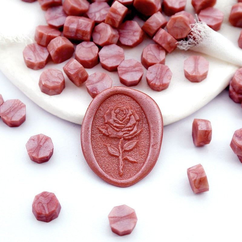 Some rose pink wax beads placed on white cushion and cloth, and an wax seal created with them.