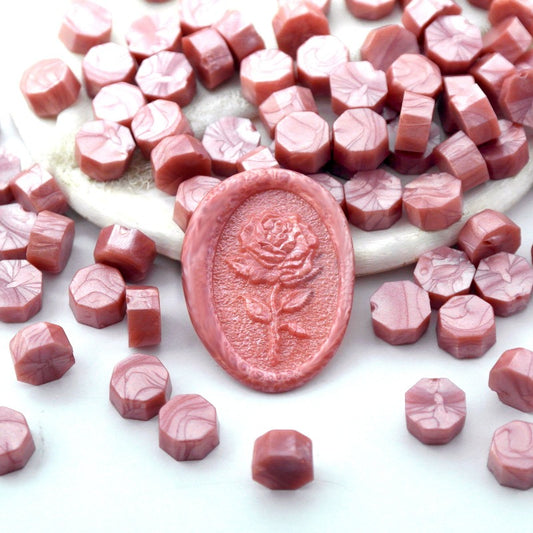 Some rose gold pink wax beads placed on white cushion and cloth, and an wax seal created with them.