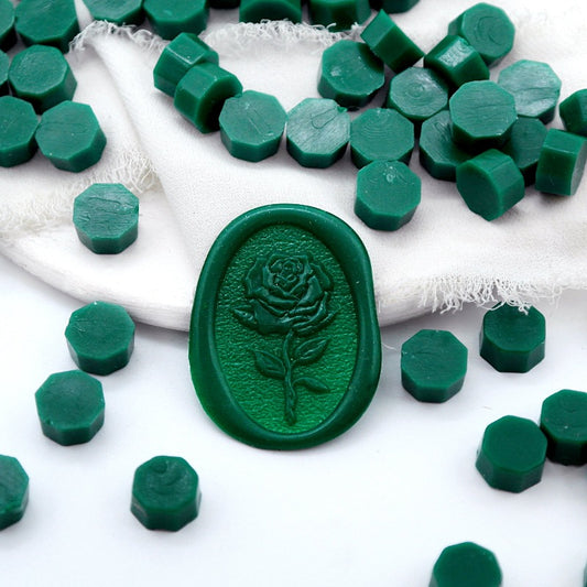 Some dark green wax beads placed on white cushion and cloth, and an wax seal created with them.