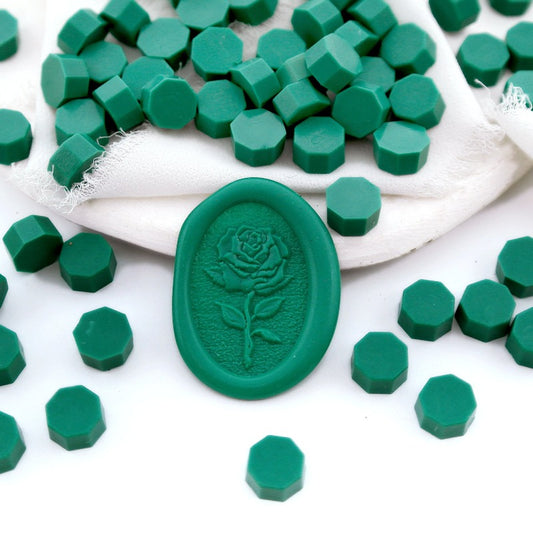 Some emerald green wax beads placed on white cushion and cloth, and an wax seal created with them.