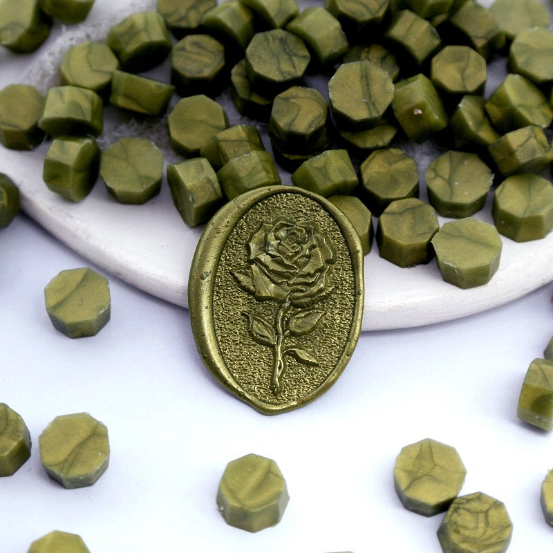 Some metallic army green wax beads placed on white cushion and cloth, and an wax seal created with them.