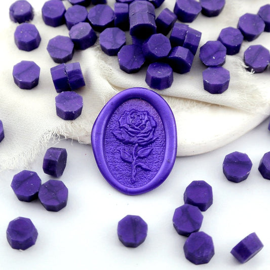 Some metallic purple wax beads placed on white cushion and cloth, and an wax seal created with them.