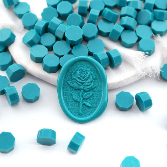 Some teal blue wax beads placed on white cushion and cloth, and an wax seal created with them.