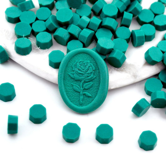 Some teal green wax beads placed on white cushion and cloth, and an wax seal created with them.