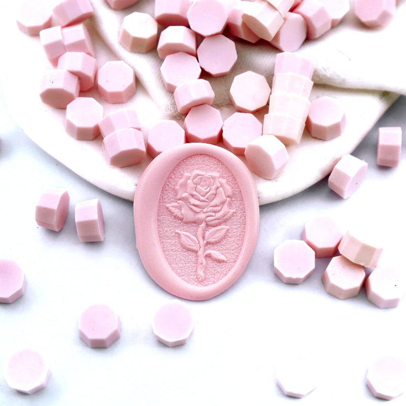 Some blush pink wax beads placed on white cushion and cloth, and an wax seal created with them.