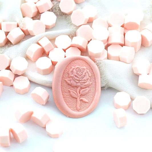 Some pale pink wax beads placed on white cushion and cloth, and an wax seal created with them.