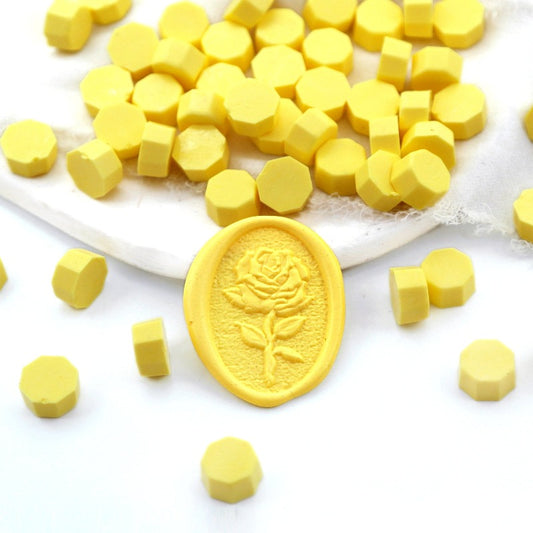 Some light yellow wax beads placed on white cushion and cloth, and an wax seal created with them.