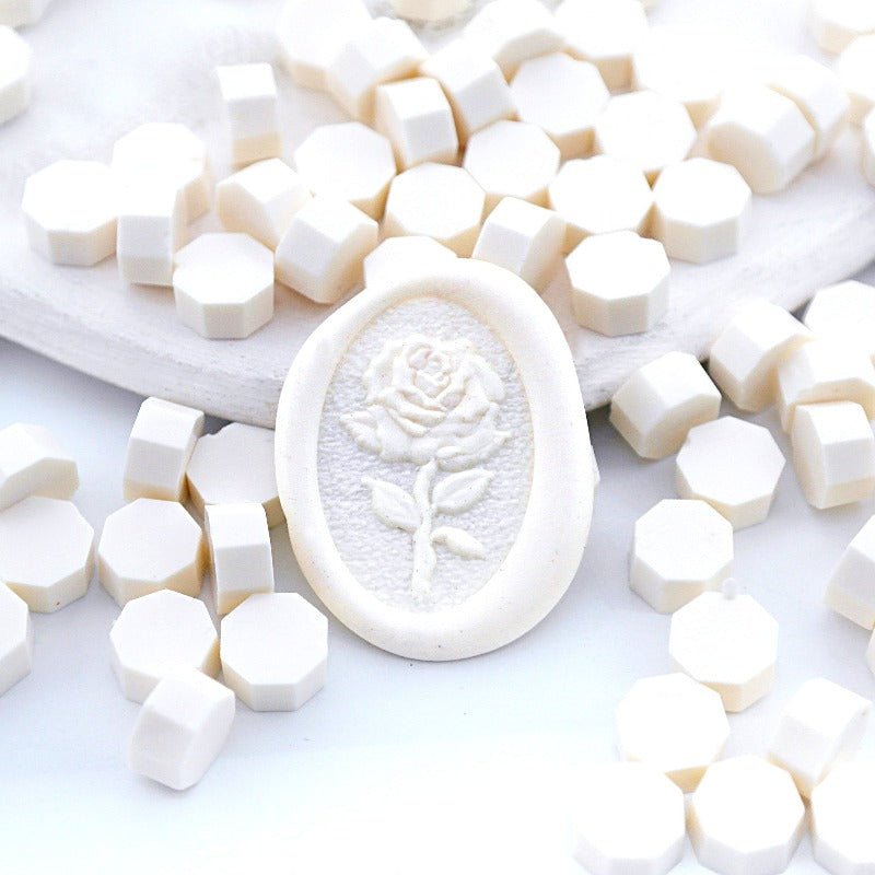 Some cream wax beads placed on white cushion and cloth, and an wax seal created with them.