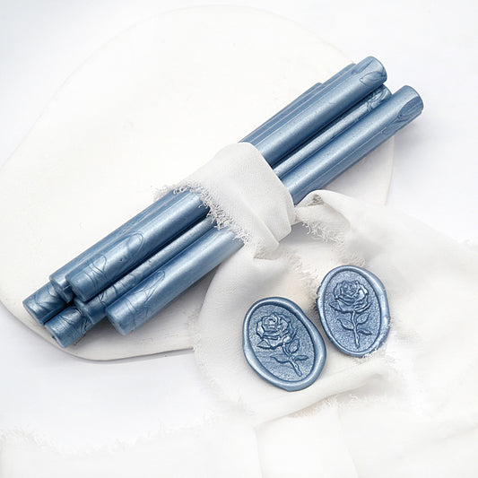 Sealing Wax Sticks in Pearlescent Dusty Blue with white wedding packing cloth wrapped, beside them, two rose flower pattern wax seals samples created.