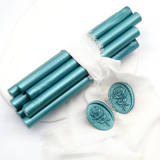 Sealing Wax Sticks in Pearlescent Dark Teal with white green wedding packing cloth wrapped, beside them, two rose flower pattern wax seals samples created.
