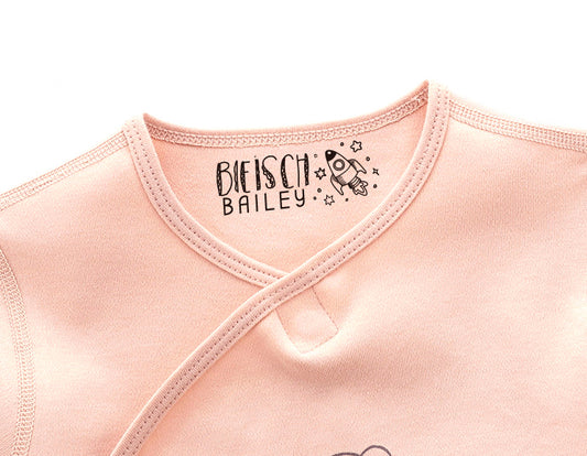 custom fabric stamp imprinted on a pink baby clothing. A cute rocket with the custom name at it's left side.
