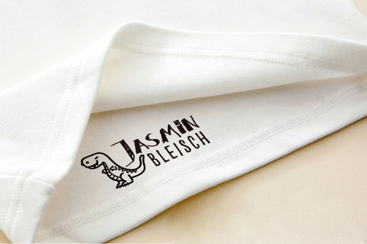 Custom Clothing Stamp, imprinted on a white clothes. A dinosaur at the left side of the custom name.