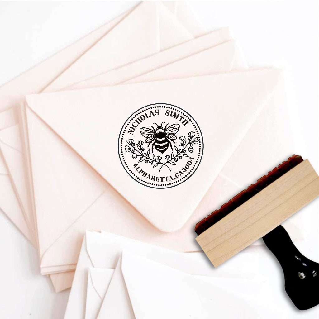 A personalized self inking address stamp, customized with your name and address, bee and flower, stamped on the pink envelope.