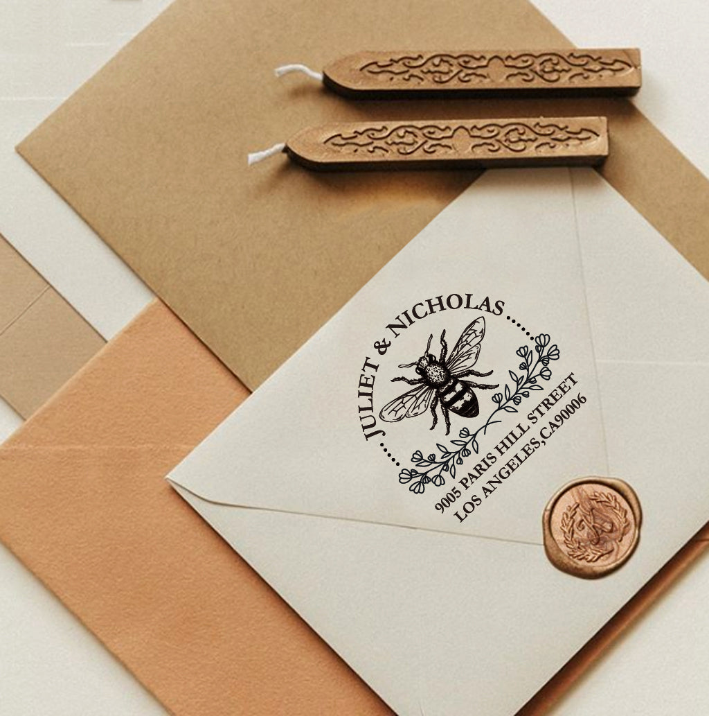 A personalized self inking return address stamp, customized with your name and address, bee and flower, stamped on the white envelope, beside it, sealing wax is creating a wax seal on the mail.