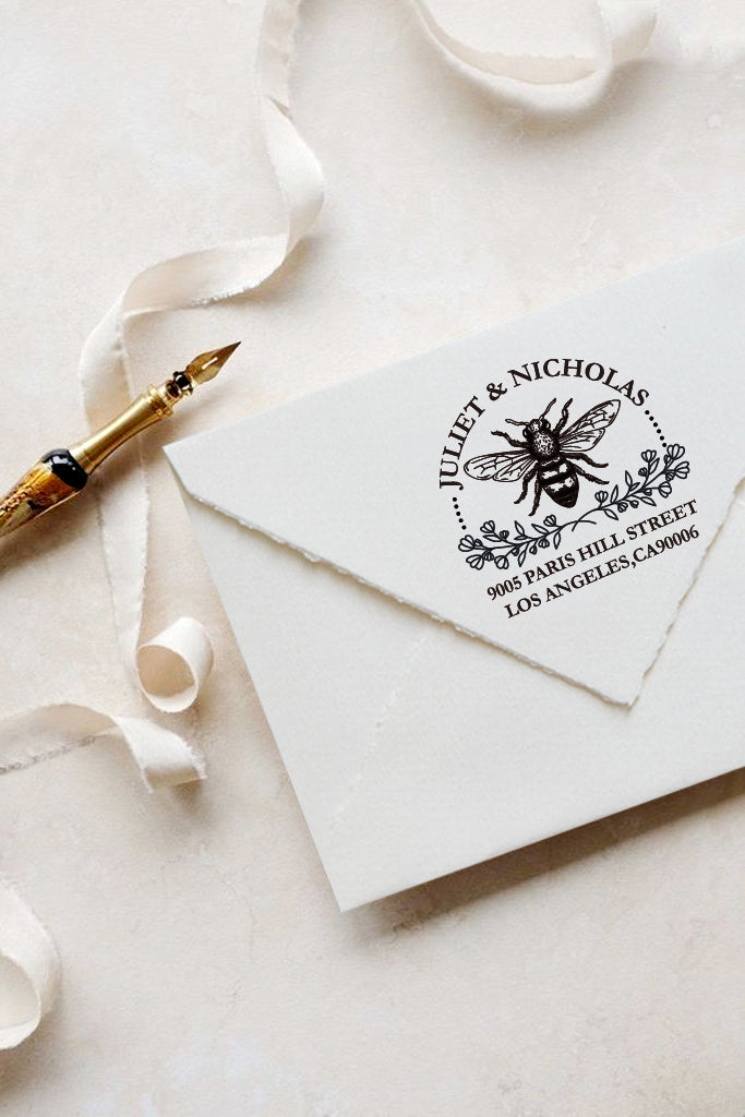 A personalized self inking address stamp, customized with your name and address, bee and flower, stamped on the white envelop, beside it, a ribbon is waiting for packing the gift.