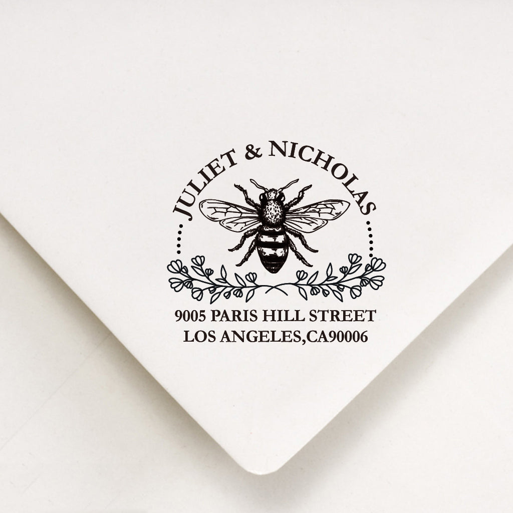 An address stamp's artwork on the white envelope. A bee in the middle and 2 branch floral under it. The custom name above the bee and make as a curve. The address under the floral.
