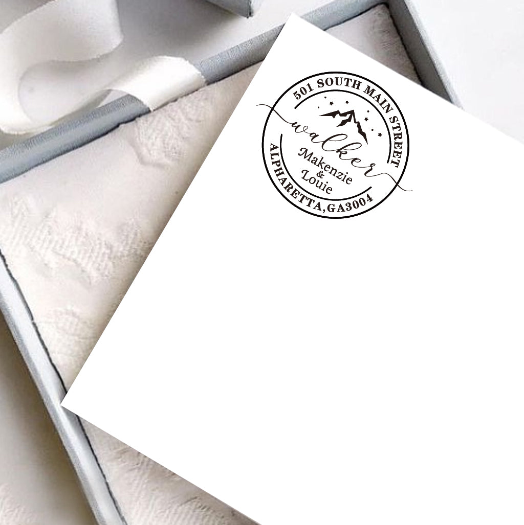 A personalized self inking address stamp, customized with your name, address and mountain, stamped on the white card, a gift box is under it.