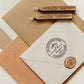 A personalized self inking return address stamp, customized with your name, address and mountain, stamped on the white envelope, beside it, sealing wax is creating a wax seal on the mail.
