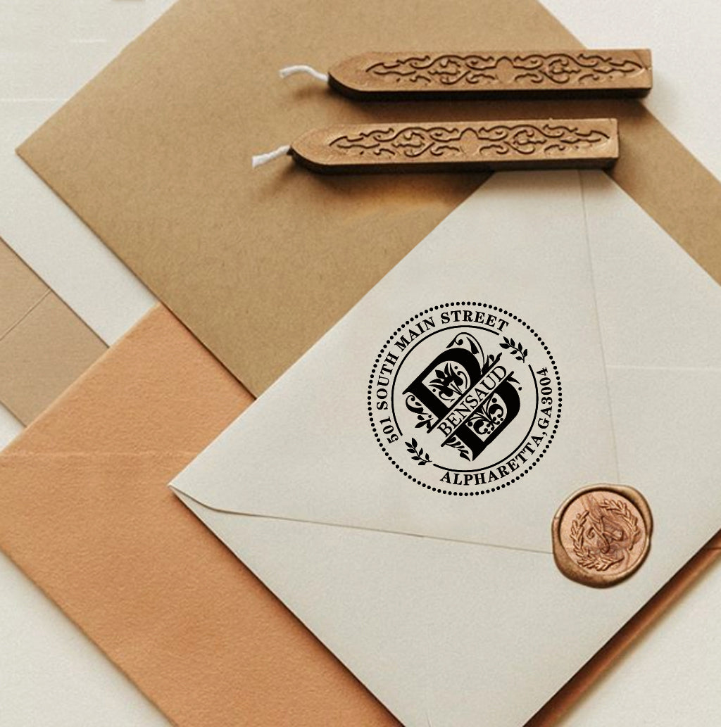 A personalized self inking return address stamp, customized with your name, address, initial and leaves, stamped on the white envelope, beside it, sealing wax is creating a wax seal on the mail.