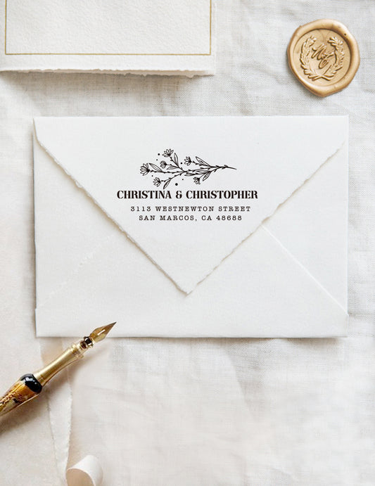 A personalized self inking wedding address stamp, customized with your name, address and flower, stamped on the white envelope, beside it, a wax seal is waiting for sealing the mail.