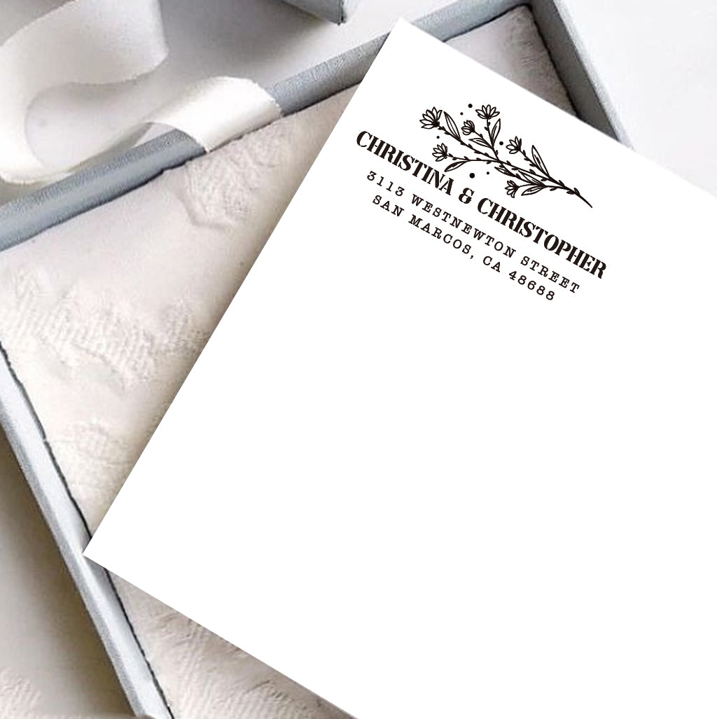 A personalized self inking address stamp, customized with your name, address and flower, stamped on the white card, a gift box is under it.