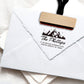 A personalized self inking return address stamp, customized with your mountain logo name and address, stamped on the white envelope.