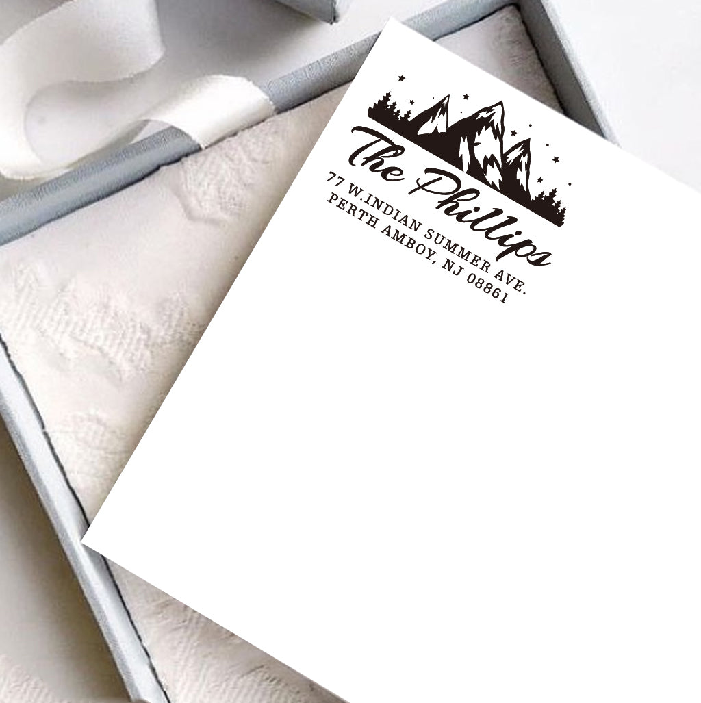 A personalized self inking address stamp, customized with your mountain name and address, stamped on the white card, a gift box is under it.