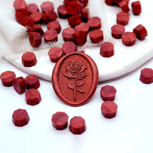 Some rich red wax beads placed on white cushion and cloth, and a rose wax seal created with them.